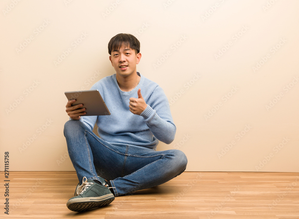 Young chinese man sitting using his tablet smiling and raising thumb up