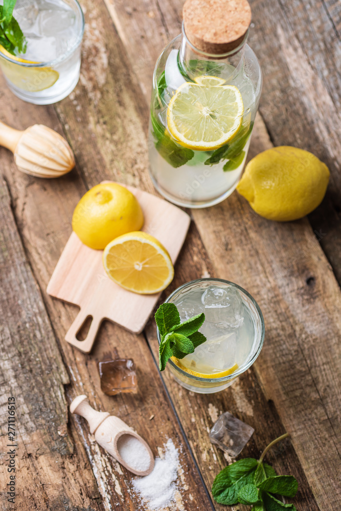 Bottle and two glasses of fresh lemonade with lemon slices, mint and ice on old wooden planks