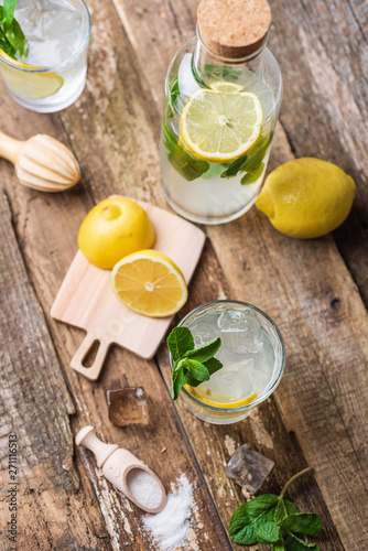 Bottle and two glasses of fresh lemonade with lemon slices  mint and ice on old wooden planks