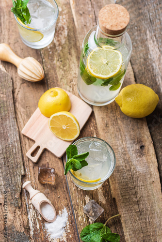 Bottle and two glasses of fresh lemonade with lemon slices, mint and ice on old wooden planks