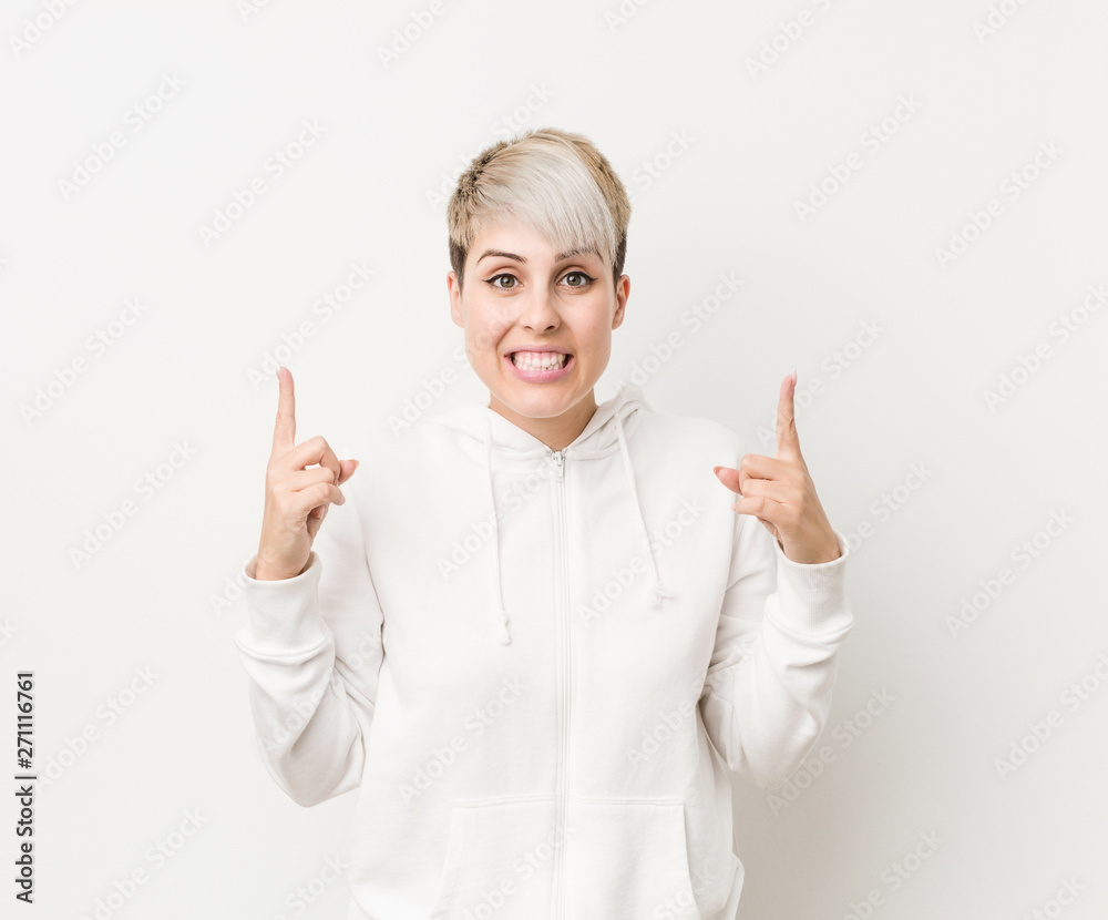 Young curvy woman wearing a white hoodie indicates with both fore fingers up showing a blank space. Young curvy woman wearing a white hoodie indicates with both fore fingers up showing a blank space.