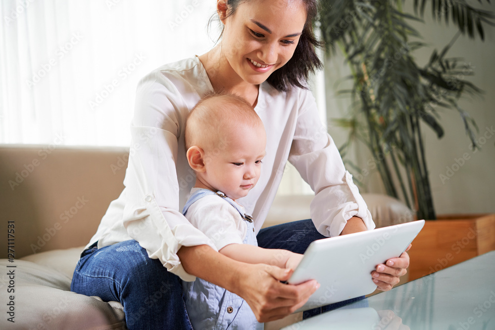 Cheerful young mixed-race woman and her little son watching animation on digital table Cheerful young mixed-race woman and her little son watching animation on digital table