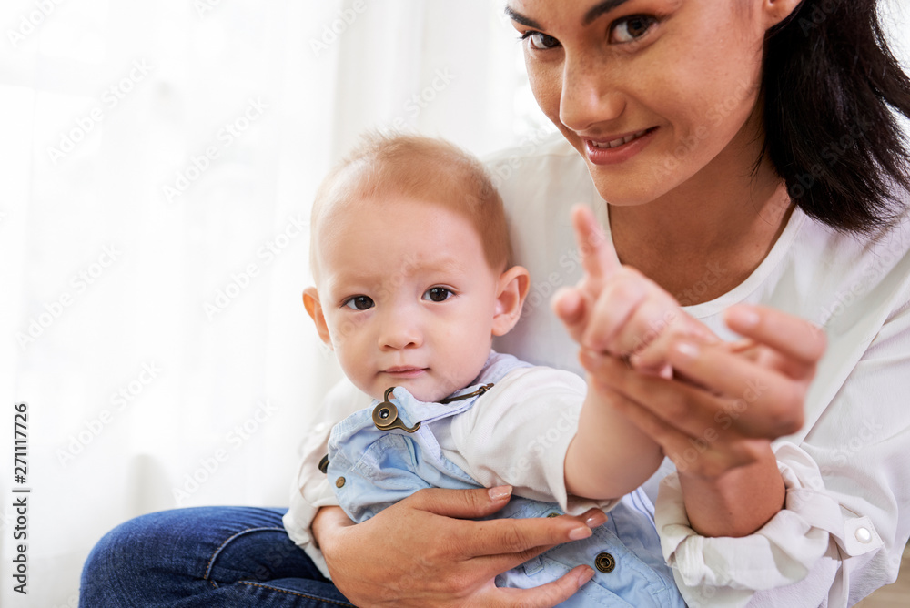 Smiling pretty mixed-race woman holding hand of her baby pointing at camera with index figer Smiling pretty mixed-race woman holding hand of her baby pointing at camera with index figer