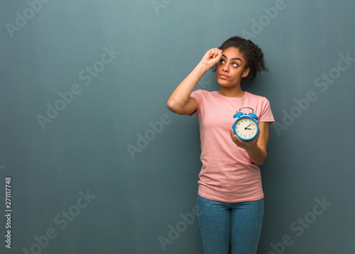 Young black woman making the gesture of a spyglass. She is holding an alarm clock. © Asier