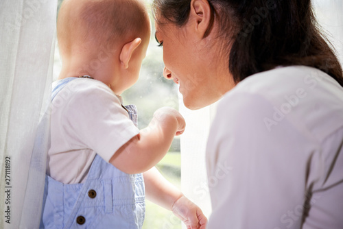 Young woman and her little son looking at the street throgh the window at home