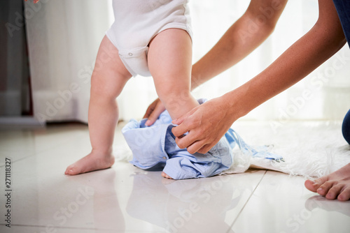 Close-up image of mother trying to dress her running baby boy in overall in the morning