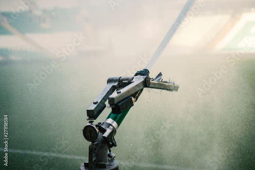 Fototapeta Naklejka Na Ścianę i Meble -  Automatic water irrigator in action. Close-up sprinkler of automatic watering. Green grass soccer field