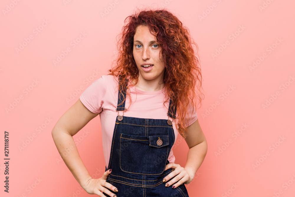 Young pretty ginger redhead woman wearing a jeans dungaree confident keeping hands on hips. Young pretty ginger redhead woman wearing a jeans dungaree confident keeping hands on hips.