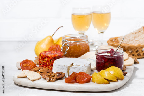 assortment of snacks - cheeses, nuts, fruits and wine on white table