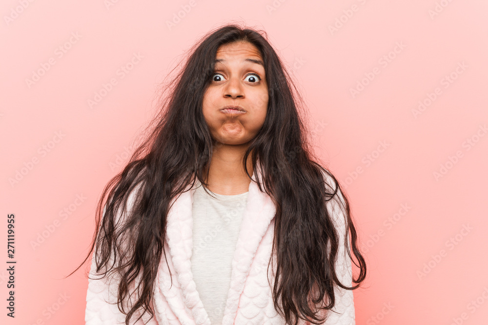 Young indian woman wearing pajama blows cheeks, has tired expression. Facial expression concept. Young indian woman wearing pajama blows cheeks, has tired expression. Facial expression concept.