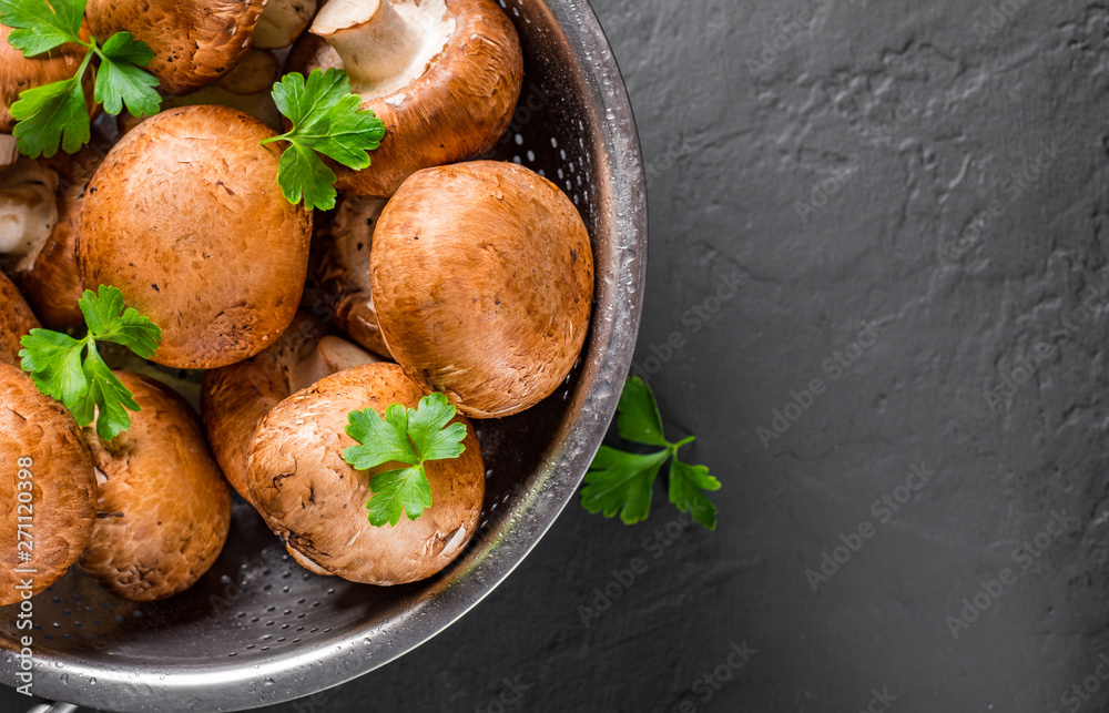 Fresh raw mushrooms champignons in stainless steel colander on Dark grey black slate background with copy space. top view Fresh raw mushrooms champignons in stainless steel colander on Dark grey black slate background with copy space. top view