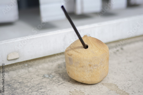 Coconut with a hole and a cocktail tube standing on a littered surface after party