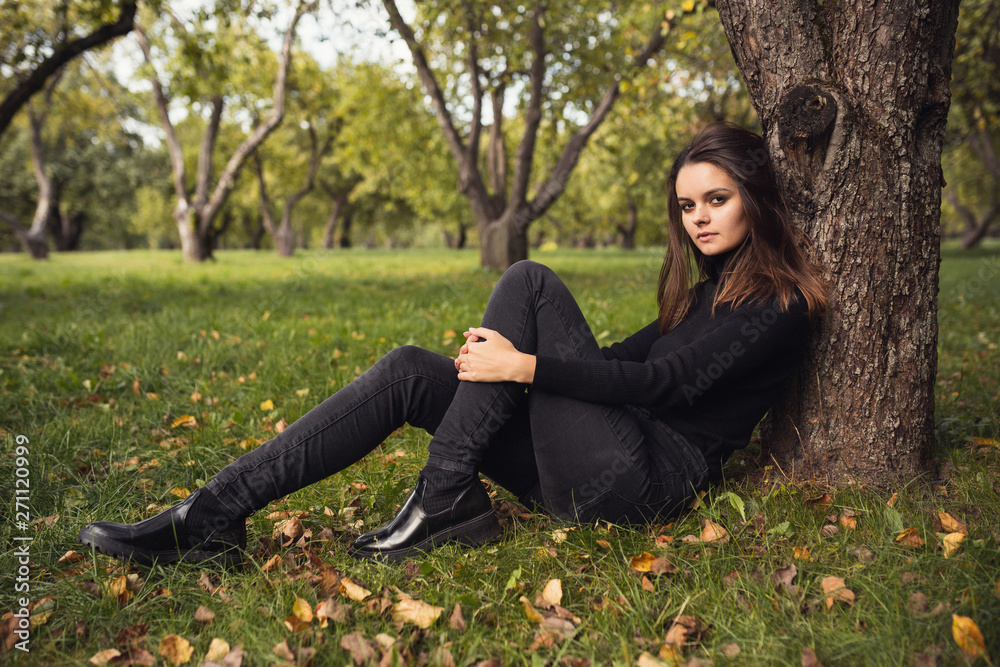 Obraz premium A beautiful young brunette walks through the autumn park in a black sweater and coat,