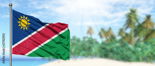 Waving Namibia flag in the sunny blue sky with summer beach background. Vacation theme, holiday concept. photo