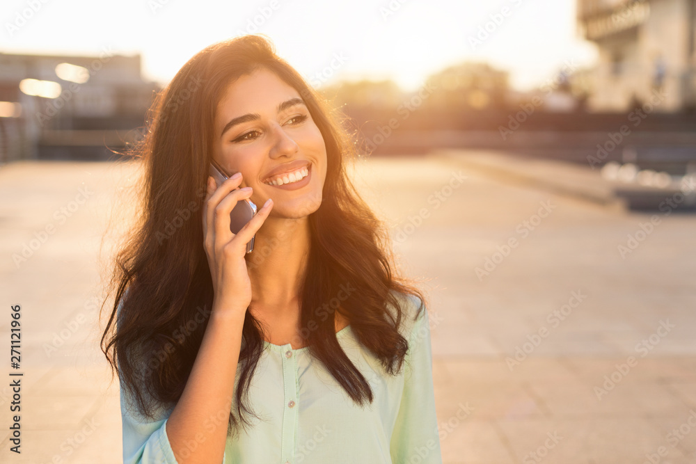Happy female student talking on phone, walking at sunset in city Happy female student talking on phone, walking at sunset in city
