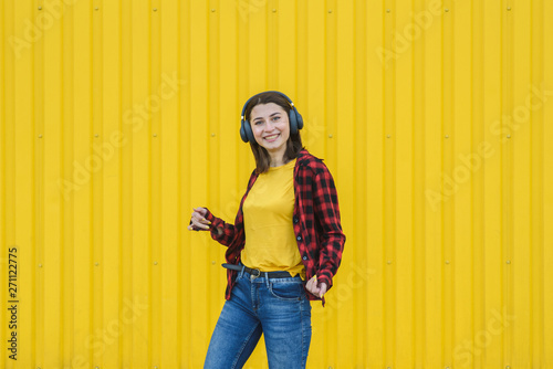 Happy girl listening to music on the street over yellow background