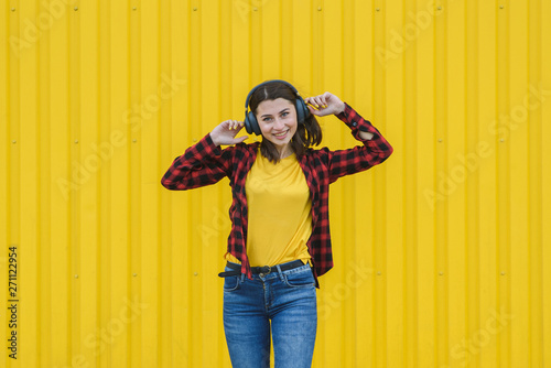 Happy girl listening to music on the street over yellow background