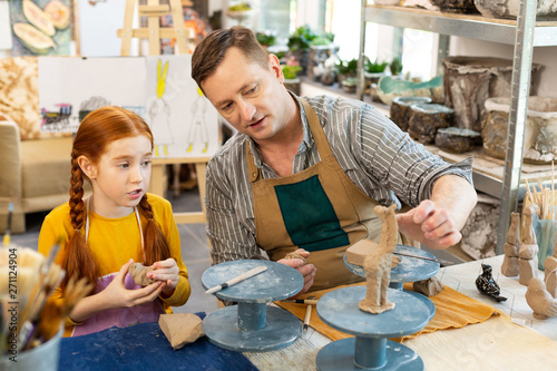 Fotografie Cute red-haired girl asking her art teacher questions about clay