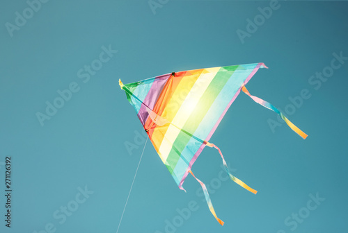 Rainbow colored kite flying in clean blue sky. Freedom and summer holiday