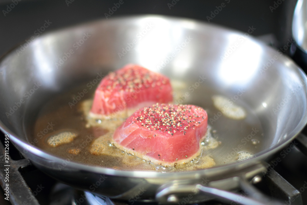 Ahi tuna steaks searing in a stainless steel pan on a gas stove. Stock