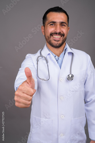 Handsome bearded Persian man doctor against gray background