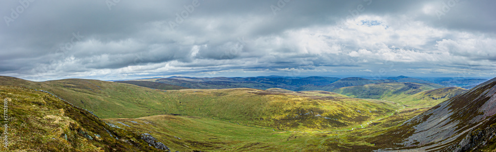 A panorama view of a Scottish mountain valley with heather and stream under a stormy huge white clouds sky