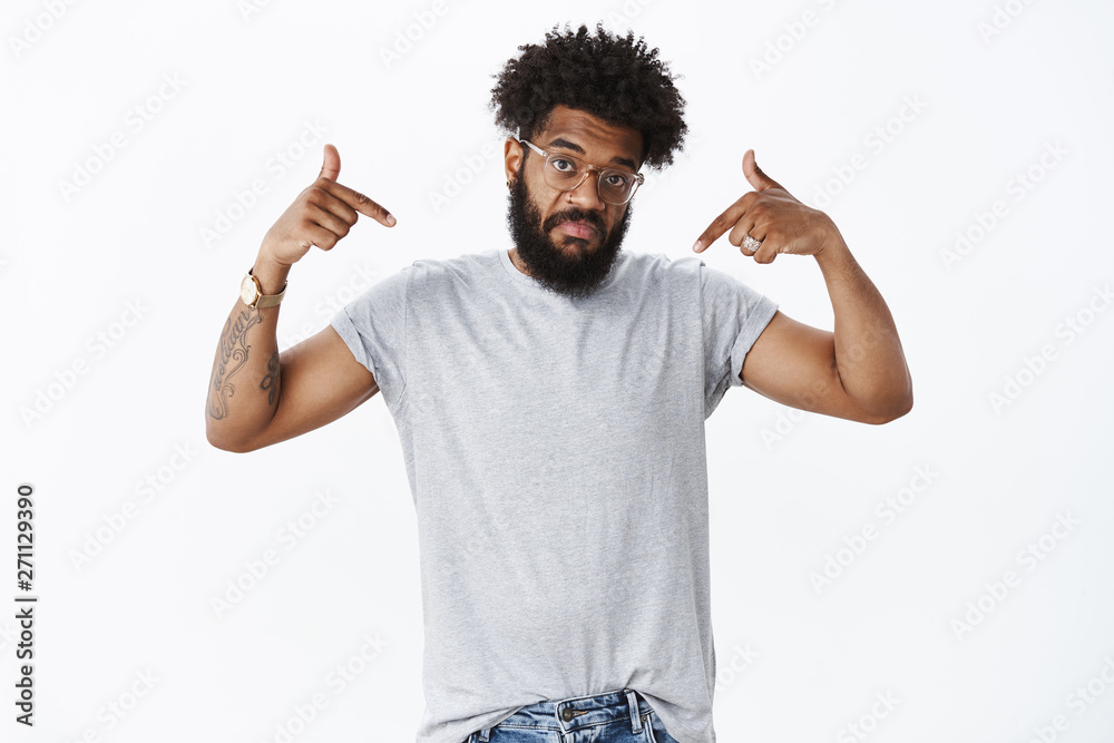Portrait of adult african american man with beard and curly hair in glasses pointing at himself with not bad expression, pulling chin up and raising eyebrows questioned and unsure, hearing opinion Portrait of adult african american man with beard and curly hair in glasses pointing at himself with not bad expression, pulling chin up and raising eyebrows questioned and unsure, hearing opinion
