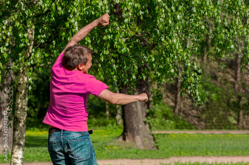 Handsome, sporty guy jumping in the park. Young man in pink t-shirt.