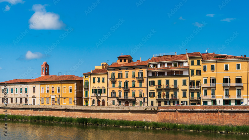 Colorful old houses along the bank of the Arno river. Cityscape in Pisa, Italy on a sunny summer day.