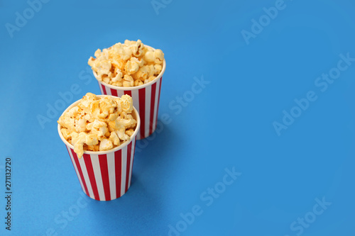 two striped white and red paper cups with fragrant crispy popcorn stand one after another on a light blue background, copy space