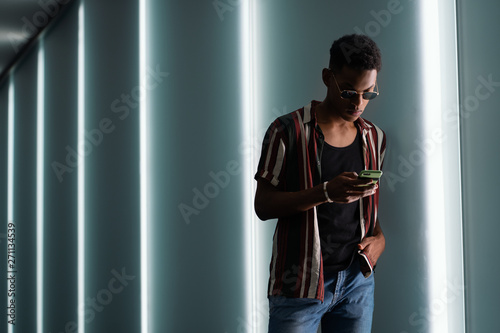 young handsome attractive guy in sunglasses poses in the neon light of the night city and uses his mobile phone