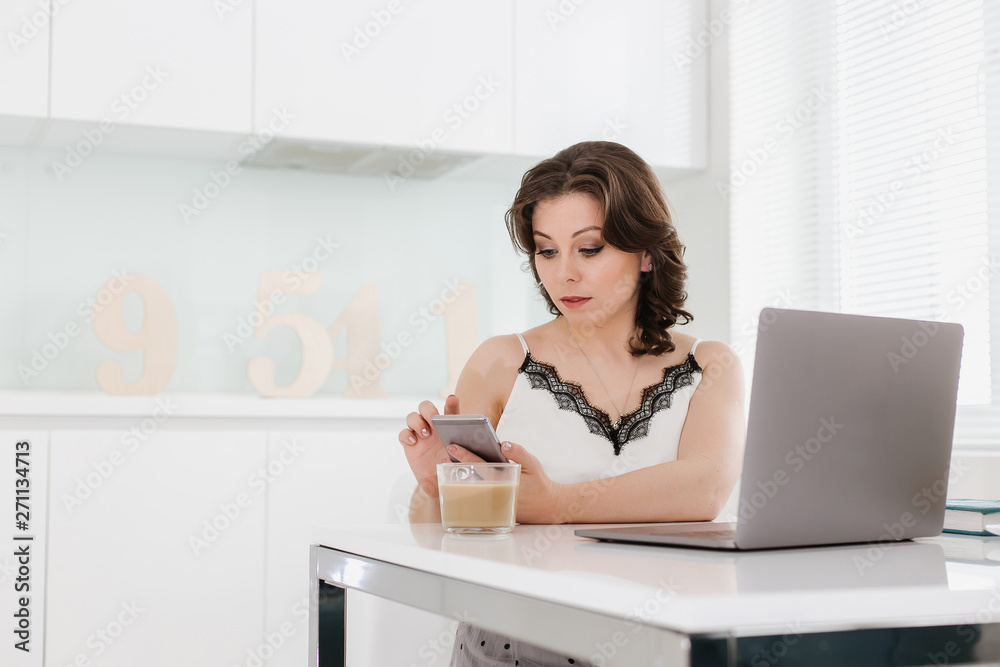A beautiful young Caucasian woman sits at a table in a white room (kitchen), with a laptop, diary and office supplies on the table. On a blurred background - numbers. Woman is a numerologist A beautiful young Caucasian woman sits at a table in a white room (kitchen), with a laptop, diary and office supplies on the table. On a blurred background - numbers. Woman is a numerologist
