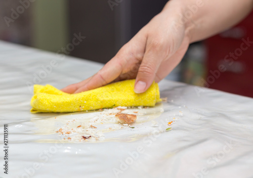 woman washes the kitchen table with a yellow rag