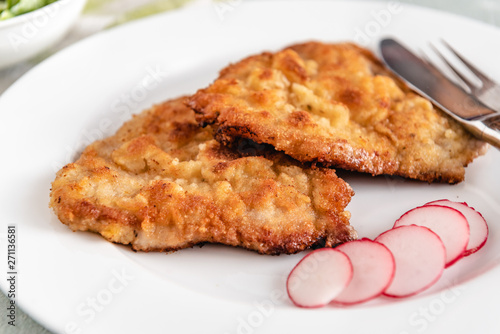 Fried pork chop in breadcrumbs served with radishes.