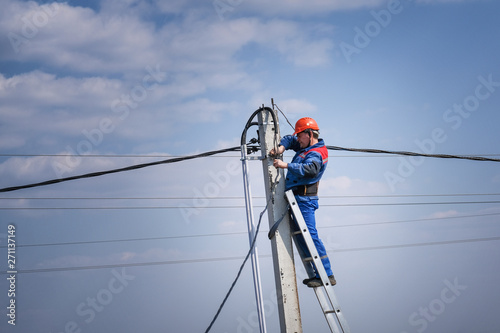 electrical engineer performs wiring on a high pole standing on the stairs. high-rise electrical work. podkluchenie house to the power lines