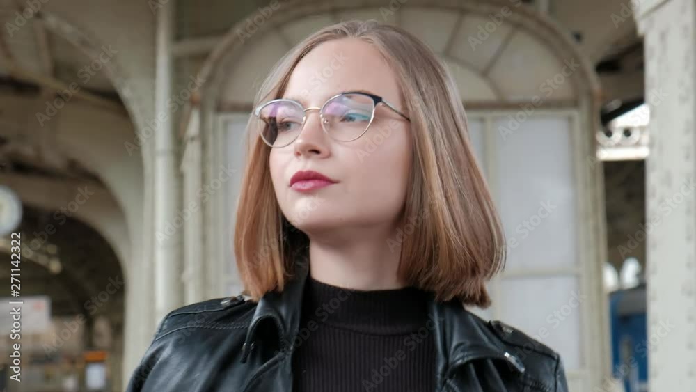 Attractive red-haired young woman with short haircut, wearing glasses and black leather jacket is standing at beautiful historic Vitebsk railway station in St. Petersburg and waiting for train. Attractive red-haired young woman with short haircut, wearing glasses and black leather jacket is standing at beautiful historic Vitebsk railway station in St. Petersburg and waiting for train.