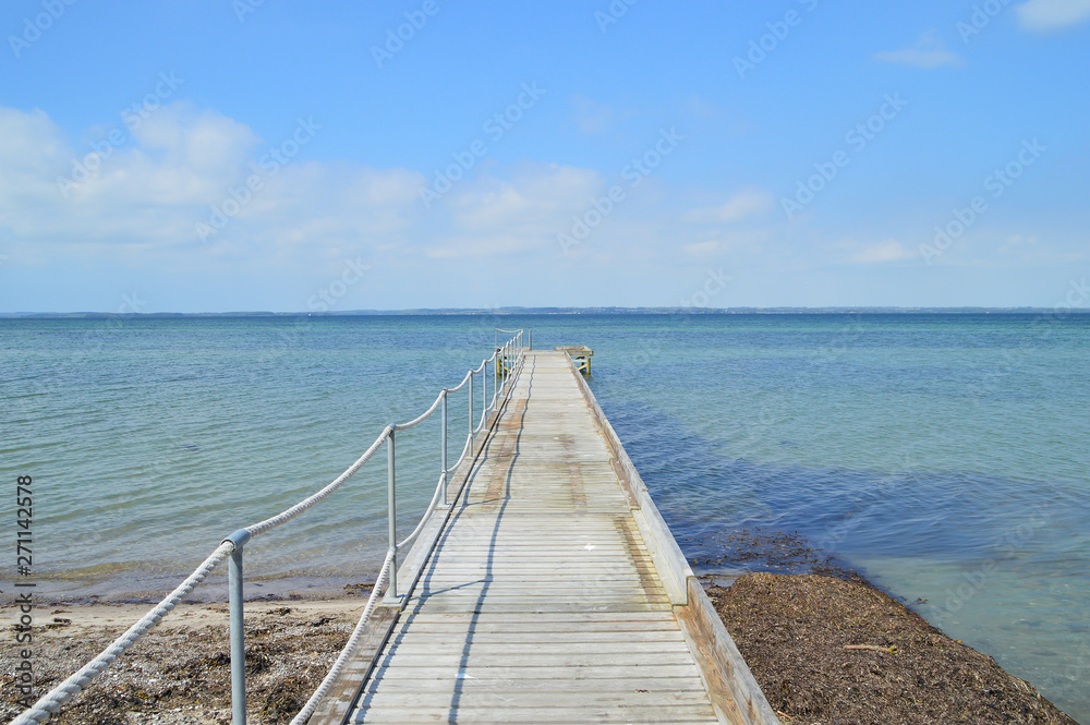 Empty dock, calm sea and sky background. View of wooden bridge above smooth ocean.