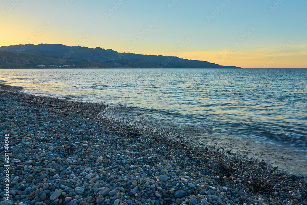 The sunset on the pebble beach with hills on the background, Kolymbari, Crete, Greece.