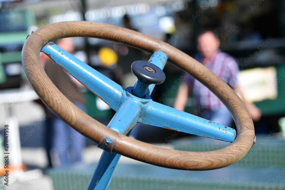 Detail view of the wooden steering wheel of a historical tractor. In the background, an elderly farmer goes for a walk. Detail view of the wooden steering wheel of a historical tractor. In the background, an elderly farmer goes for a walk.