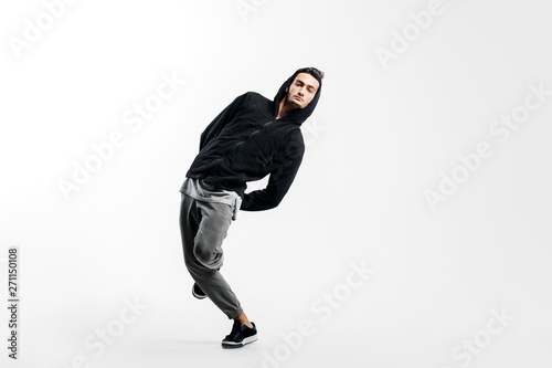 Stylish young man wearing a black sweatshirt and gray pants is dancing street dances on a white background