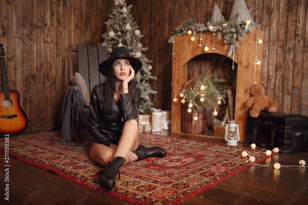 Fototapeta premium Beautiful young woman in sexual black lingerie and black hat posing in Christmas decorations.