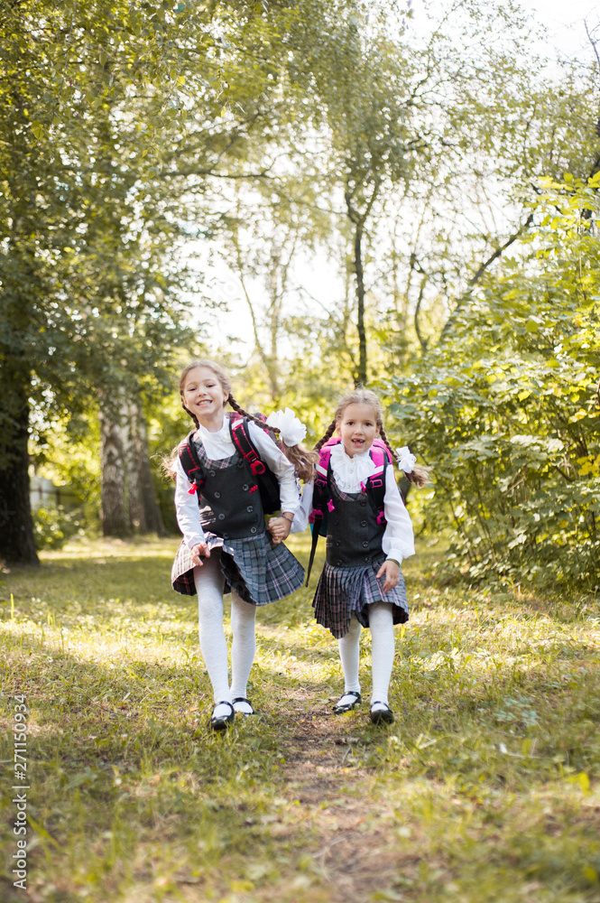 Two schoolgirls with backpacks on their shoulders run along the path in the park. Two schoolgirls with backpacks on their shoulders run along the path in the park.