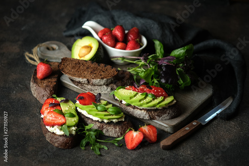 Healthy breakfast sandwich with avocado, cheese, strawberries, herbs and seeds on a dark background. An idea for bruschetta or for a healthy snack. Healthy vegan breakfast.
