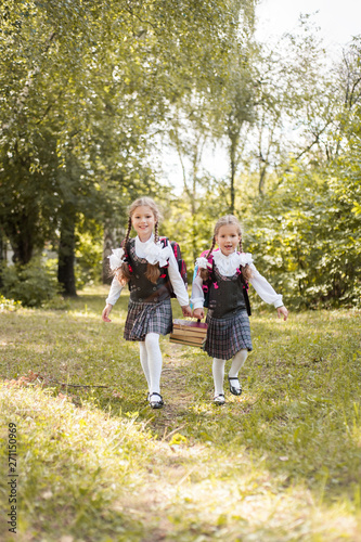 Two schoolgirls carry a stack of books along the path in the park.
