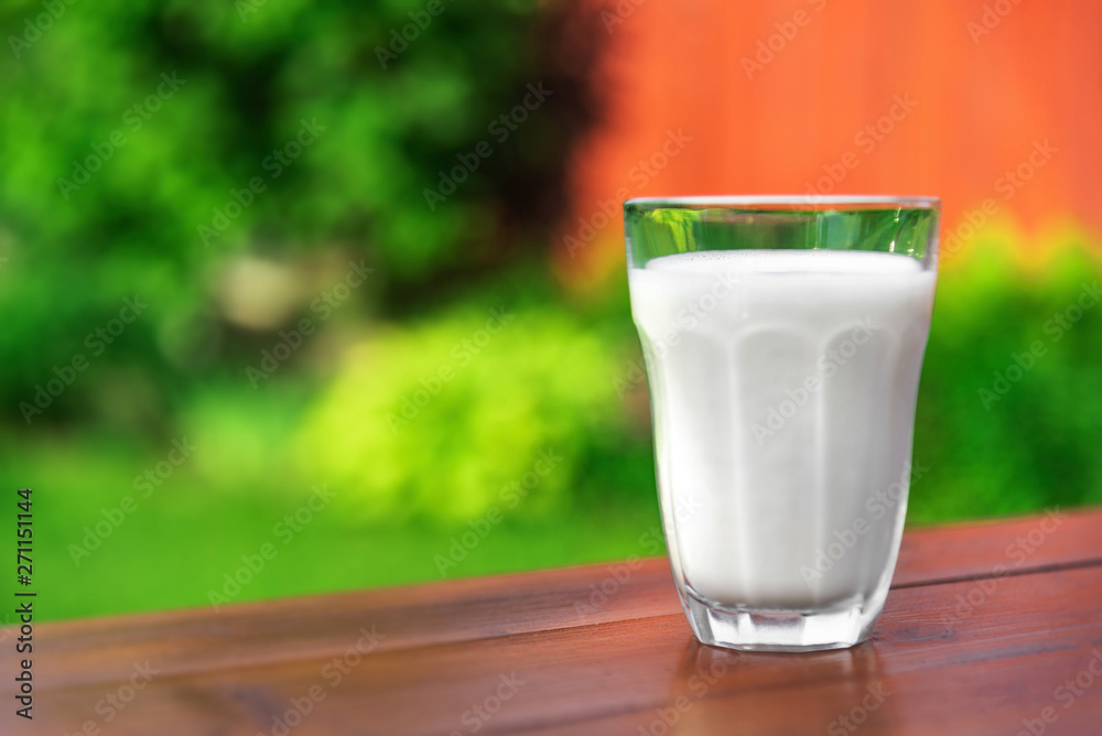 A glass of milk on the background of the summer garden on a wooden table. A glass of milk on the background of the summer garden on a wooden table.
