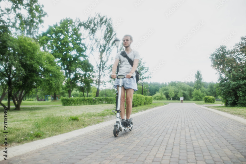 Fototapeta premium man in shorts on an electric scooter with a backpack riding through a city park