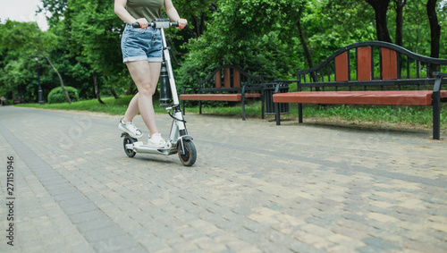 young woman driver of electric scooter in city park. ecological transport