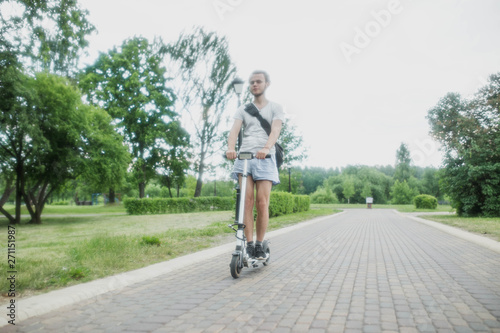 man in shorts on an electric scooter with a backpack riding through a city park