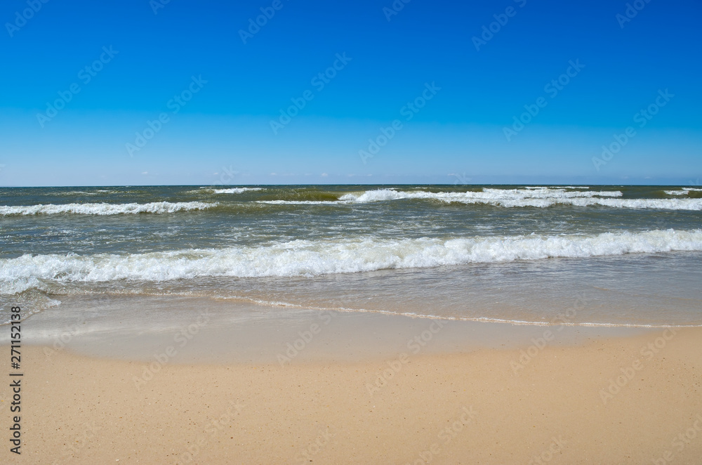 Sea waves wash the clean sandy beach. Landscape on a wild beach. The sea in the summer.