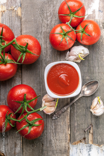 Ketchup or tomato sauce, garlic and fresh tomatoes on a branch on a rustic background. Top view